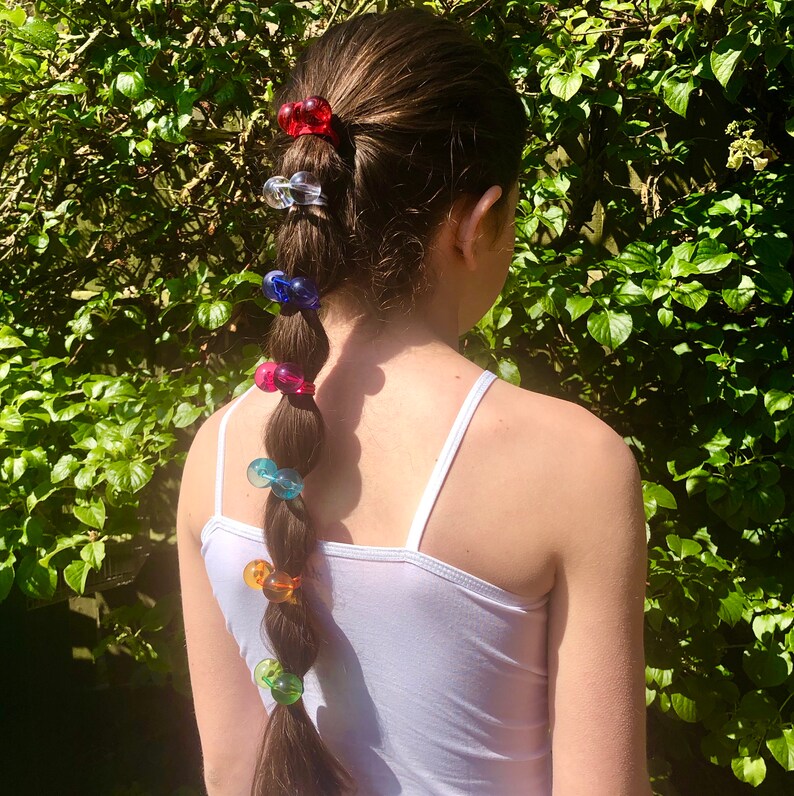 May include: A braided ponytail with colorful plastic hair clips. The clips are in various colors, including red, blue, green, and pink.