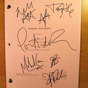 May include: A pink script from the television show "Arrested Development" with multiple signatures in black ink. The script is titled "Pilot" and lists the writer and directors. The Imagine Television and 20th Century Fox Television logos are also visible.