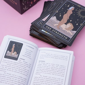 May include: A book with a black and white illustration of a woman with a lion on the cover. The book is titled "The Strength" and is part of a tarot deck. The text on the page describes the meaning of the Strength card in both upright and reversed positions.