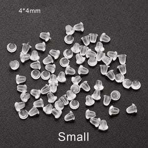 Peut inclure: Un ensemble de petits fermoirs d'oreilles transparents, d'environ 4 mm, dispersés sur une surface sombre. Le mot "Small" est imprimé en blanc en bas de l'image.
