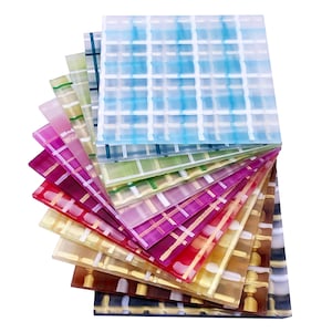 May include: A selection of square decorative tiles in a fan arrangement. Each tile displays a grid pattern in shades of blue, green, pink, and brown. The translucent material allows light to pass through, creating a vibrant display of colours.