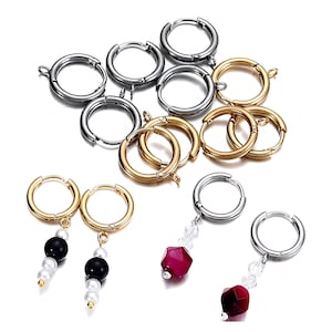 May include: A collection of hoop earrings in gold and silver colours. Some earrings have dangling features, including black and white beads, clear crystals, and faceted red gemstones. The earrings are displayed on a white surface.