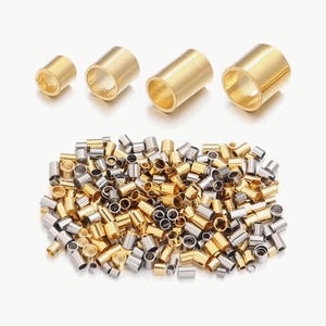 May include: A collection of small, cylindrical metal crimp beads in gold and silver tones. Four larger, individual gold-colored cylinders are arranged in a row above a large pile of mixed-size gold and silver metallic tube beads.