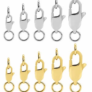 Può includere: Una collezione di dieci chiusure a moschettone disposte su due file. La fila superiore presenta cinque chiusure in metallo color argento di dimensioni graduate, mentre la fila inferiore mostra cinque chiusure in metallo color oro di dimensioni corrispondenti.