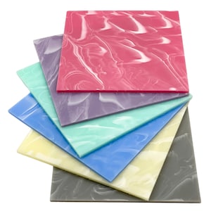 Puede incluir: Un conjunto de seis láminas cuadradas de plástico marmoleado de diferentes colores. Las láminas están dispuestas en forma de abanico, con la lámina superior de color rosa, seguida de morado, azul claro, amarillo, gris y gris oscuro.