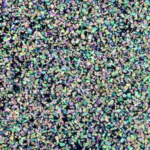 Op de afbeelding: Een close-up van iriserende glitter met een mix van groene, blauwe en paarse tinten. De glitter is verspreid over een zwarte achtergrond.