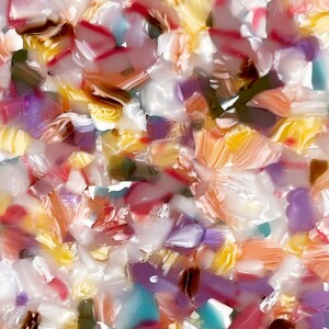 Op de afbeelding: Een close-up van een kleurrijk, abstract patroon gemaakt van kleine, onregelmatige stukjes materiaal. De stukjes zijn in een willekeurig patroon gerangschikt en zijn voornamelijk wit, geel, roze en paars.