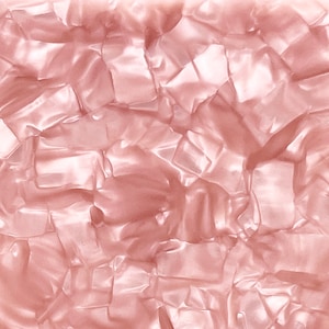 May include: A close-up of a pink, iridescent, textured surface. The surface is made up of irregular, geometric shapes that reflect light, creating a shimmering effect. The overall appearance is smooth and glossy.
