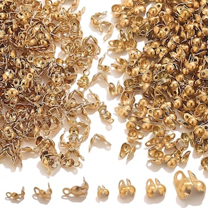 May include: A selection of small, gold-coloured metal findings, including crimp end caps and other jewellery-making components. The findings are scattered across a white surface, showcasing their various shapes and sizes, perfect for crafting.