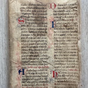 May include: A page from an old book with handwritten text in black ink on parchment paper. The text is in Latin and is surrounded by red and blue decorative borders. The page number is 2 at the top left corner and 10 at the top right corner.