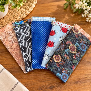 May include: Five rectangular fabric pouches with metal squeeze frames arranged in a fan shape. The pouches feature various patterns including a tan mottled print, black and white paw prints, blue polka dots, light blue cat faces, and a dark floral print.