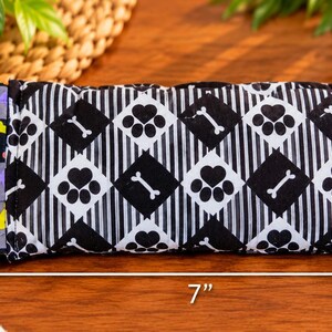 May include: A rectangular fabric pouch featuring a black and white argyle pattern with paw prints and bone icons. The side panel has a gray background with colorful bone shapes. The pouch measures 3.5 inches by 7 inches as indicated by arrows.