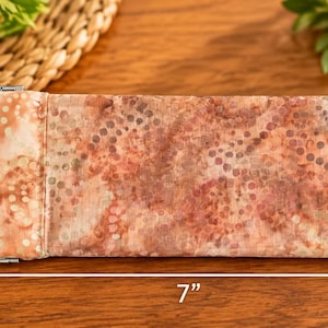 May include: A rectangular fabric eyeglass case featuring a mottled peach, brown, and cream pattern with small circular motifs. The case has a metal squeeze-top closure and measures 3.5 inches in height by 7 inches in width as indicated by arrows.