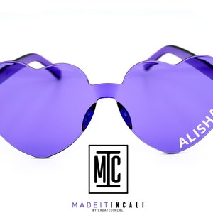 Puede incluir: Gafas de sol de color morado en forma de corazón con el nombre "ALISHA" impreso en la lente derecha. Las gafas de sol están hechas por MadeItInCali.