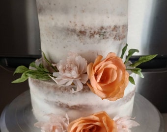 Puede incluir: Un pastel desnudo de dos niveles decorado con glaseado de mantequilla y flores de papel naranja y blanco. El pastel está sobre un soporte para pasteles plateado.