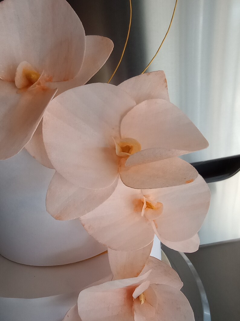 Puede incluir: Un pastel blanco decorado con delicadas flores de orqu&iacute;dea de color melocot&oacute;n. Las flores est&aacute;n dispuestas en cascada, creando un aspecto rom&aacute;ntico y elegante.