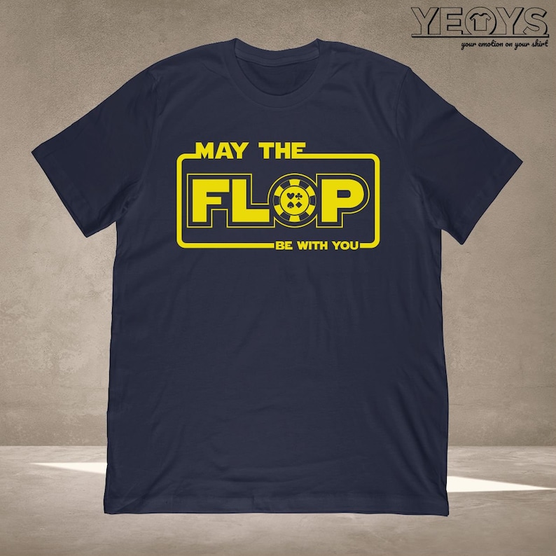 Puede incluir: Una camiseta azul marino con un gr&aacute;fico amarillo que dice "Que el Flop est&eacute; contigo". El gr&aacute;fico presenta una ficha de p&oacute;quer amarilla con una pica, un coraz&oacute;n, un diamante y un tr&eacute;bol negros.