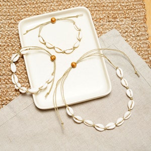May include: Three necklaces made of white seashells and brown wooden beads on a white plate. The necklaces are made of string and have adjustable lengths.