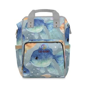 May include: A baby backpack with a light blue background and a pattern of blue and orange fish. The backpack has a gray handle and straps, with the text "TJO BABY" on the front pocket.