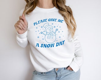 May include: White sweatshirt with blue text that reads "Please give me a snow day" and a cartoon snowman graphic.