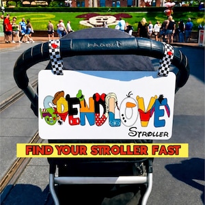 May include: A white stroller tag with the words "SEND LOVE" in colorful, cartoon-style letters. The tag also has the text "FIND YOUR STROLLER FAST" in a yellow banner. The stroller handle has a black and white checkered flag.