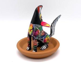 May include: A black wooden figurine of a dog with colorful floral patterns painted on its body. The dog is sitting on a small brown clay dish.
