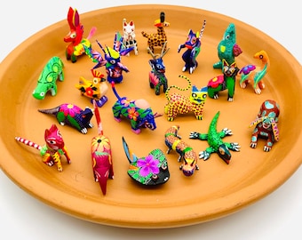 May include: A collection of 20 hand-painted wooden animal figurines. The figurines are brightly colored and feature a variety of animals, including a cat, a giraffe, a bird, a lizard, and a fish. The figurines are arranged on a terracotta plate.