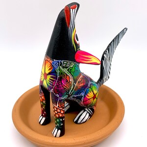 May include: A black wooden dog figurine with colorful floral patterns and white accents. The dog is sitting on a terracotta dish.