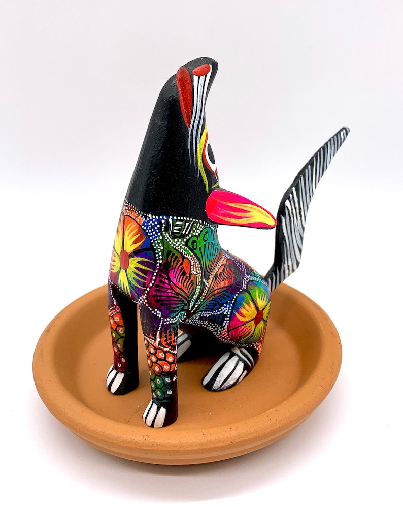 May include: A black wooden dog figurine with colorful floral patterns and white accents. The dog is sitting on a terracotta dish.