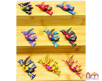 May include: Eight colorful wooden lizard figurines with intricate painted details. Each lizard is painted in a different color combination, including blue, green, purple, red, yellow, and black. The lizards are arranged on a tiered wooden display.