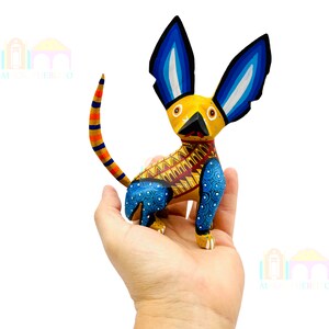 May include: A hand-painted wooden dog figurine with blue, yellow, and red details. The dog has large ears and a patterned body.