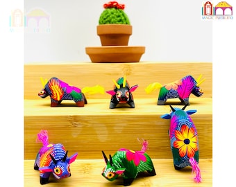 Pode incluir: Cinco figurinhas de touro de madeira coloridas com desenhos pintados intrincados. Os touros estão em várias poses e têm acentos amarelos, rosas, azuis, verdes e pretos. As figurinhas estão dispostas em uma tela de madeira de vários níveis.
