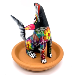 May include: A black wooden dog figurine with colorful floral patterns and a white and black striped tail. The dog is sitting on a terracotta clay dish.