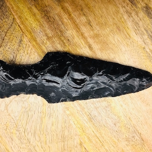 May include: A black obsidian arrowhead with a pointed tip and a smooth, polished surface.
