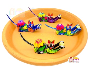 May include: Four colorful hand-painted wooden cat figurines on a terracotta plate. Each cat is holding a ball and has a long tail. The cats are painted in shades of blue, purple, green, and black with intricate details.