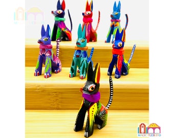 May include: A collection of vibrantly painted wooden cat figurines. Each cat features unique patterns and colors, including blue, green, red, and purple, with detailed floral and geometric designs. The figurines are displayed on a wooden surface.