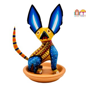 May include: Hand-painted wooden figurine of a yellow dog with blue ears and a red tongue, sitting on a terracotta base. The dog has a blue and yellow patterned body.