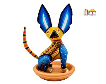 May include: Hand-painted wooden figurine of a yellow dog with blue ears and a red tongue, sitting on a terracotta base. The dog has a blue and yellow patterned body.