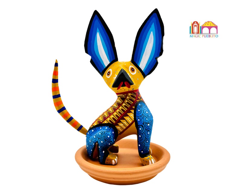 May include: Hand-painted wooden figurine of a yellow dog with blue ears and a red tongue, sitting on a terracotta base. The dog has a blue and yellow patterned body.