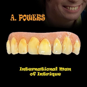 May include: A set of yellowed prosthetic teeth with a gum-coloured base, against a black background. The text "A. POWERS" and "International Man of Intrigue" are in orange and yellow, respectively, above and below the teeth.