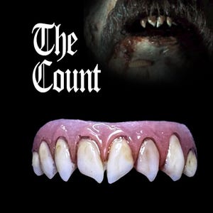 Può includere: Un set di denti finti con una linea gengivale rosa e denti giallastri e appuntiti. I denti sono disposti in fila, con le punte dei denti rivolte in avanti. Il testo "The Count" è visibile sullo sfondo.