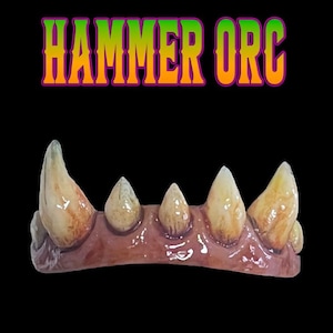 May include: A set of prosthetic teeth featuring a brown gum line and five pointed, yellowed, and stained fangs. The text HAMMER ORC is printed in a gradient of green, yellow, and orange above the teeth against a solid black background.
