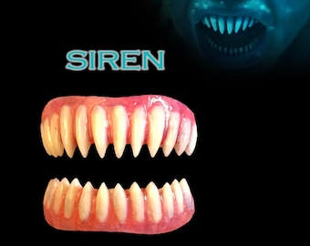 Peut inclure: Un ensemble de deux paires de dents en plastique blanc, conçues pour ressembler à des dents de sirène. Les dents sont sur une base rose et sont destinées à être portées comme un accessoire de costume. Le texte "SIREN" est écrit en lettres bleues au-dessus des dents. L'image est sur un fond noir.