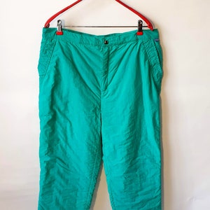 May include: A pair of teal green trousers with a button fly and side pockets. The trousers are hanging on a red hanger.