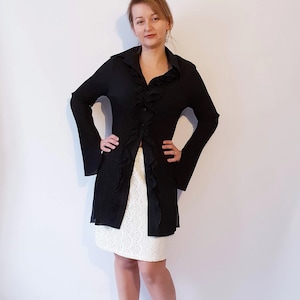 May include: A black long-sleeved shirt with a ruffled collar and a white skirt. The shirt has a button-up front and the skirt is made of lace.