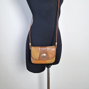 Może przedstawiać: Mała brązowa skórzana torebka na ramię z klapką i złotym zapięciem. Torebka wykonana jest z różnych odcieni brązowej skóry i ma patchworkowy wzór.