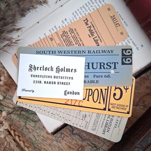 May include: A collection of vintage-style paper ephemera including a tan library card, a blue South Western Railway ticket, a yellow coupon, and a white business card printed with Sherlock Holmes Consulting Detective 221B Baker Street London.