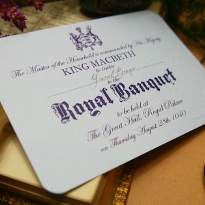 Puede incluir: Una tarjeta de invitación de color lila claro con texto adornado que anuncia un Banquete Real. El texto incluye "KING MACBETH" y "Royal Banquet" en una fuente decorativa. La invitación está fechada el 28 de agosto de 1040 e incluye un escudo real.