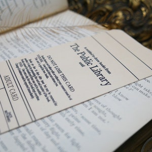 May include: A white card with black text that reads "The Public Library" and "DO NOT LOSE THIS CARD". The card is a library card for borrowing books. The card has a section for an adult card.