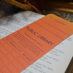 May include: An orange library card with the text "PUBLIC LIBRARY" and "This Card must be used at" printed on it. The card has a grid with the headings "DUE" and "RETURNED" for recording due dates and return dates.